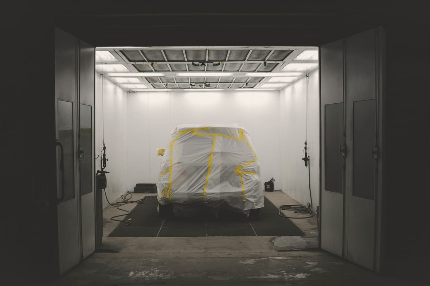 Open paint booth doors looking into a lit cabin with a masked car inside