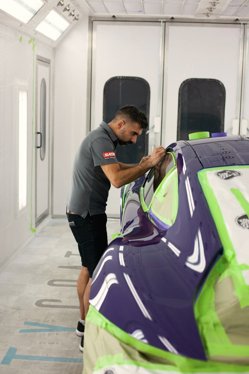 Technician taping masking paper along a car body inside a paint booth