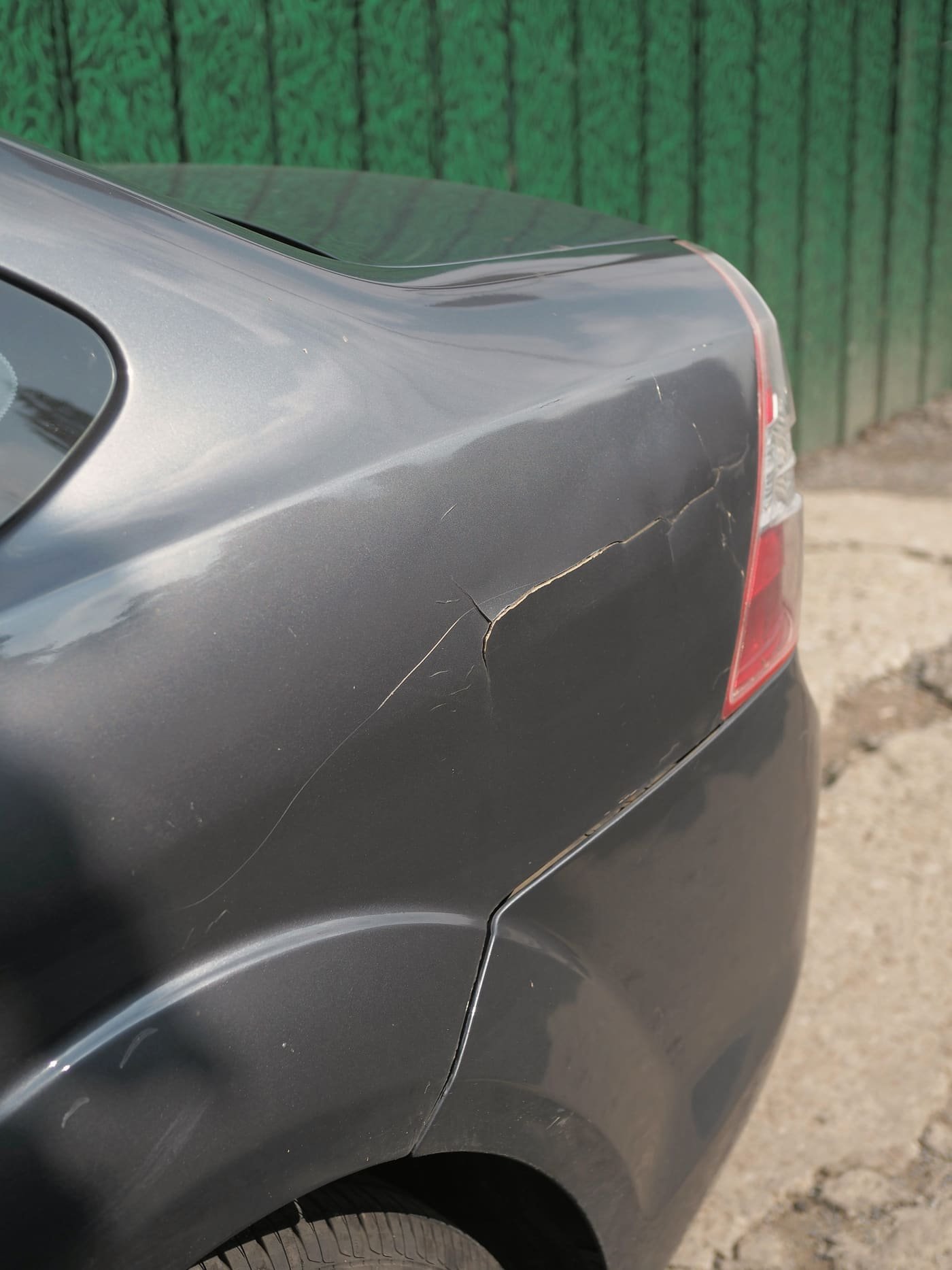 Deep crease and cracked paint running across the grey rear quarter panel of a car