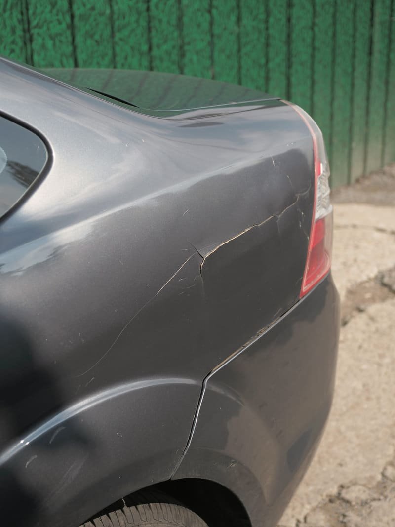 Close view of a deep crease and cracked paint running across a grey quarter panel