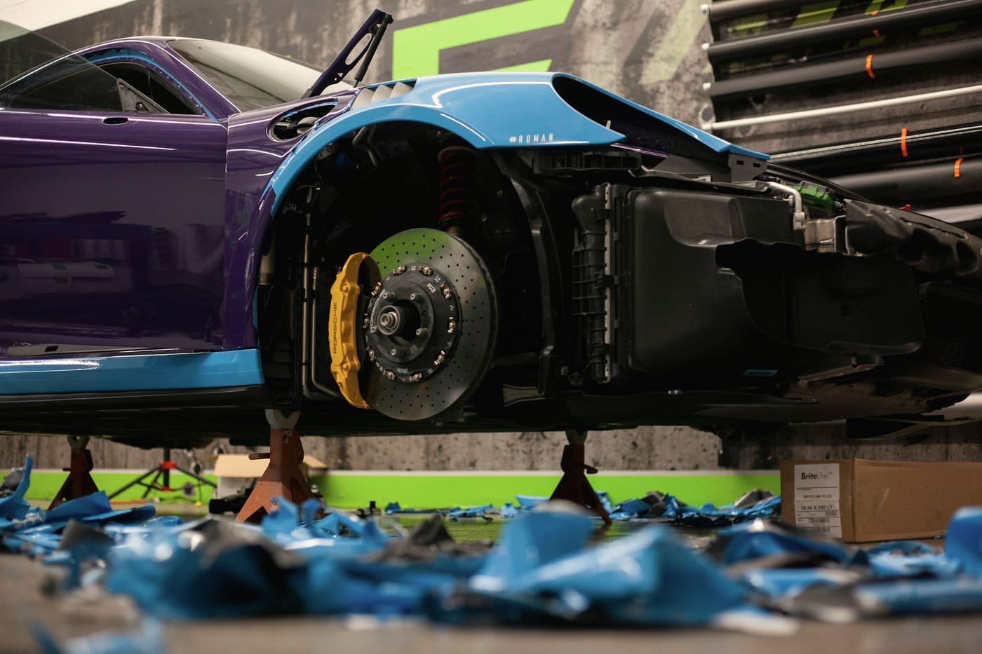 Car raised on stands with the front bumper cover removed and masking film across the floor