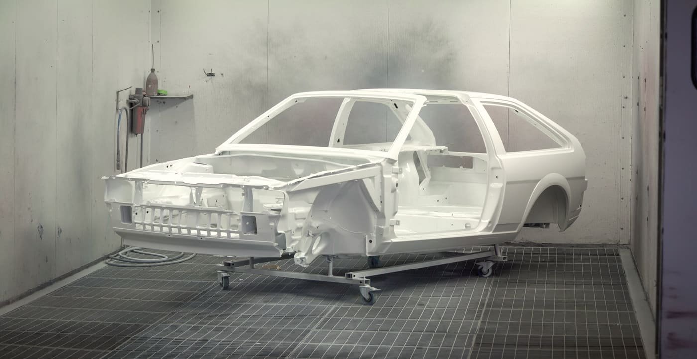 Stripped body shell coated in gray primer, standing on a workshop floor before color is sprayed