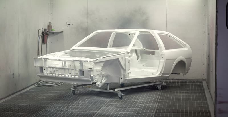 Car body in grey primer with trim removed, standing in a workshop