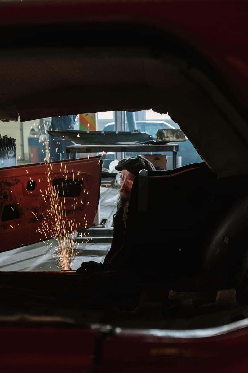 Sparks falling through the dark interior of a stripped red body shell during cutting work