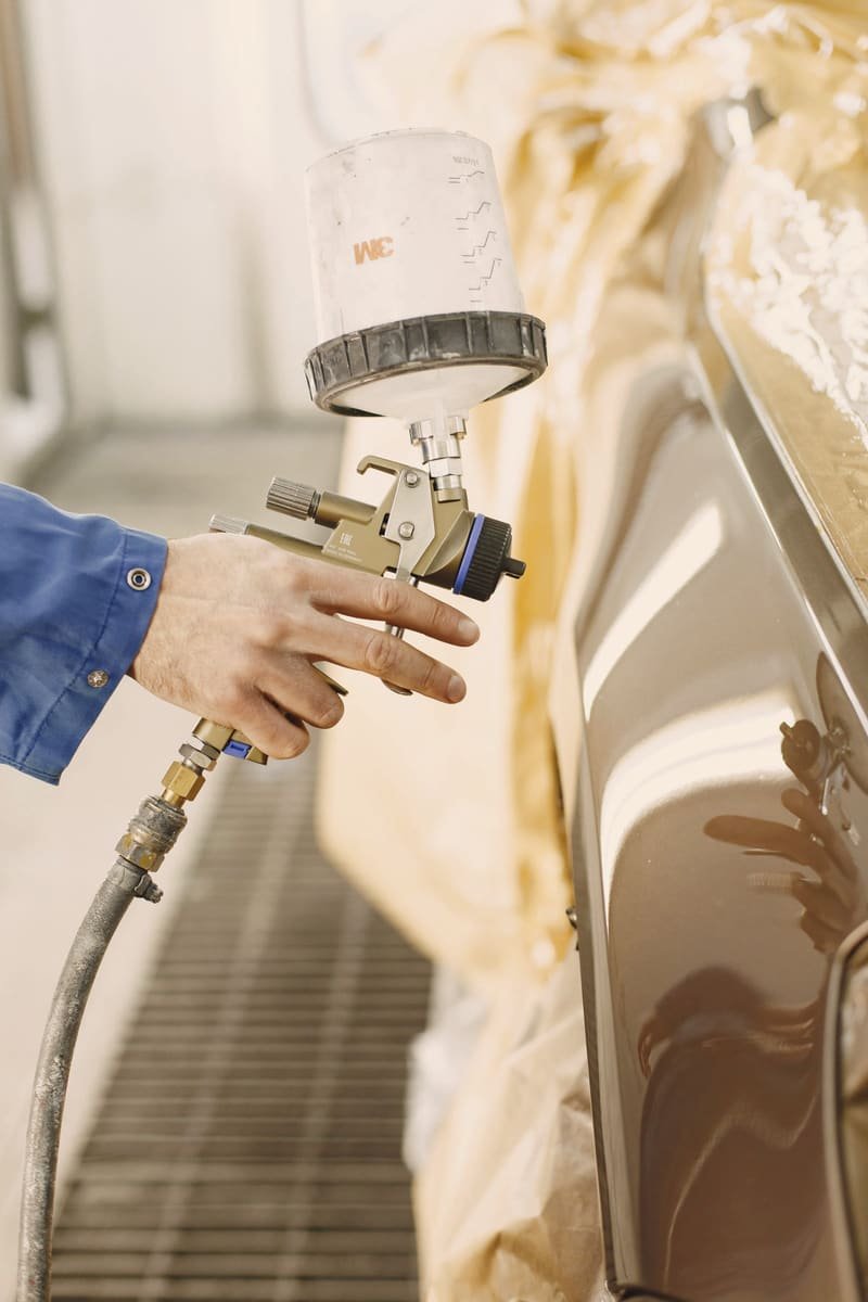 Gloved hand holding an HVLP spray gun through a pass across a panel