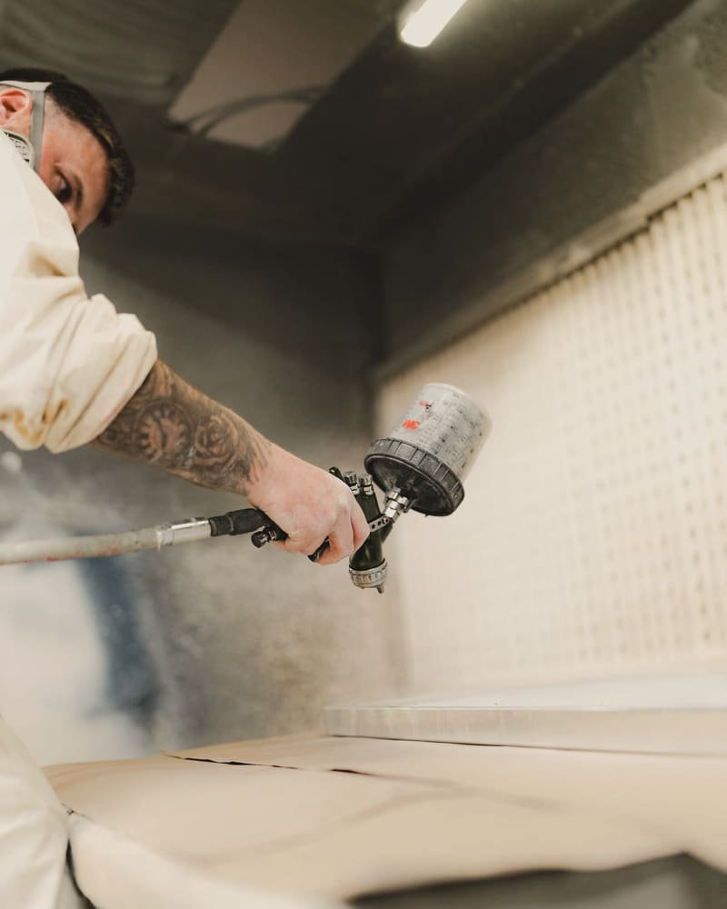Low angle view of a painter spraying a panel through heavy paint haze