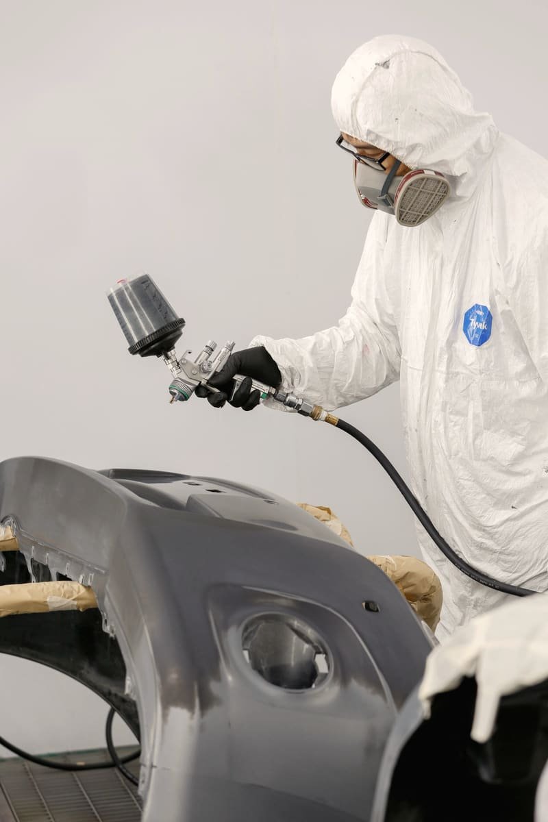 Painter in a full suit spraying primer onto a bumper cover on stands
