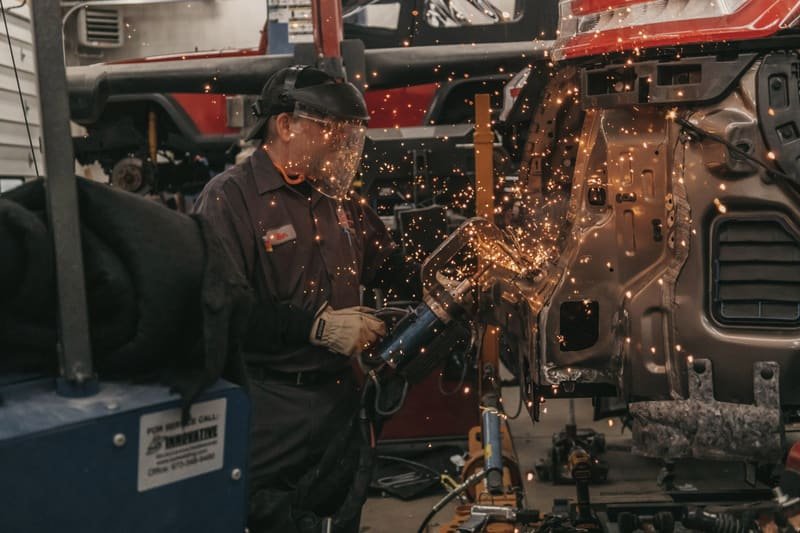 Welder in a face shield working on a stripped body shell as sparks spray